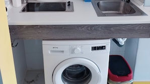 Una lavadora compacta con un panel de control, un lavamanos de acero inoxidable y un bote de basura rojo.