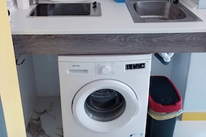 Eine kompakte Waschmaschine mit Bedienfeld, ein Edelstahl-Spülbecken und ein roter Mülleimer.