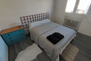 Ein Schlafzimmer mit Bett, Nachttisch, Kommode, Heizkörper und Fenster.