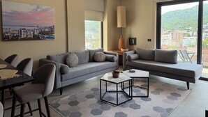 Ein modernes Wohnzimmer mit Sofa, Couchtisch und Sesseln, großen Fenstern mit Stadtblick und einem Deckenventilator.