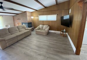 Ein Wohnzimmer mit Ecksofa, Hocker, Wand-Fernseher und Kamin.