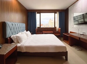 Habitación de hotel con una cama grande, un escritorio, una silla, un televisor y vistas a la ciudad desde la ventana.