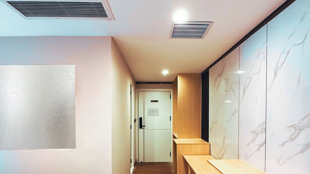 Un pasillo de hotel con una cama, un banco de madera, paredes de mármol y una alfombra estampada.