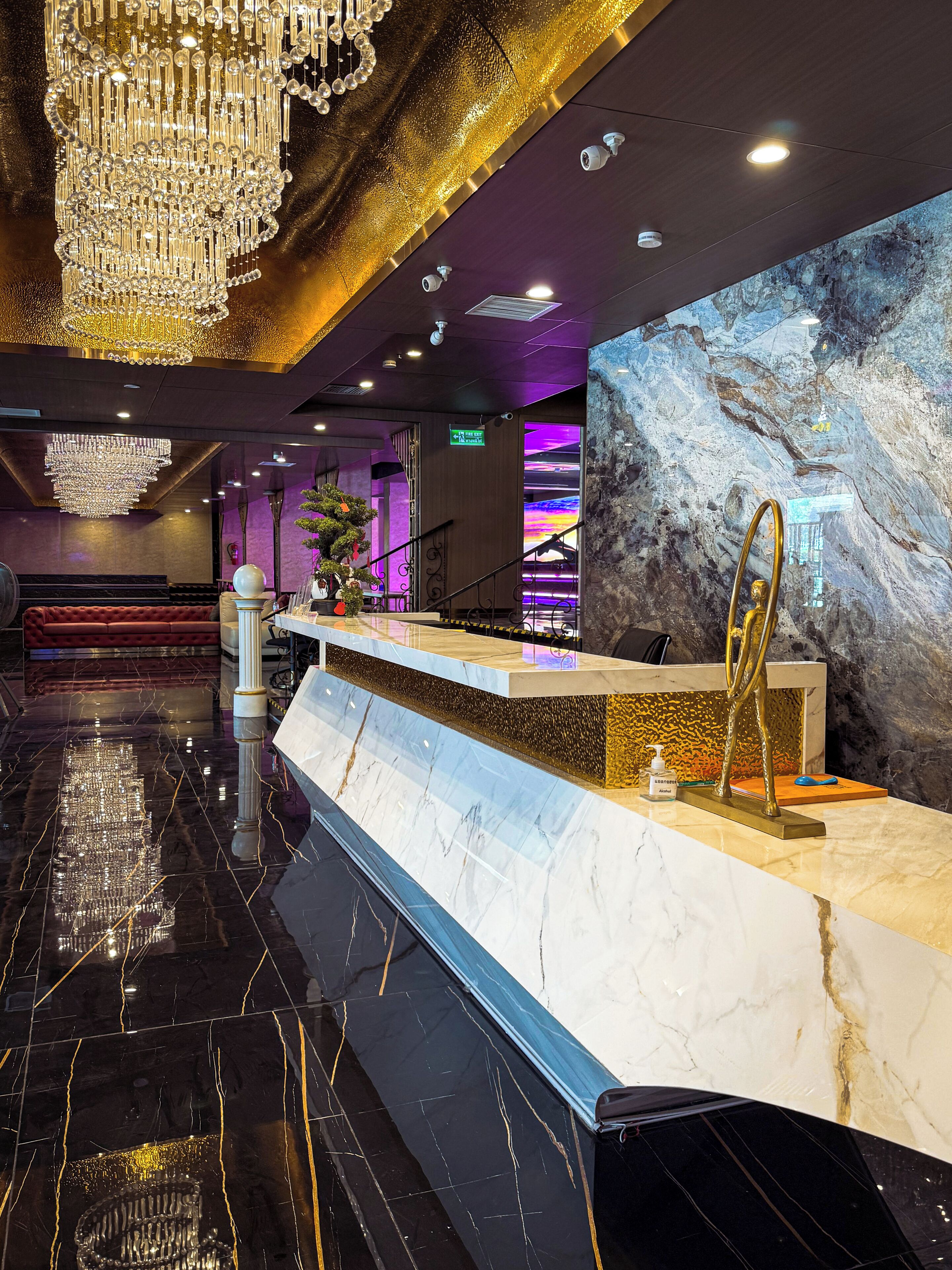 A marble reception desk with a gold accent, a chandelier, and a marble wall with a rock-like texture.