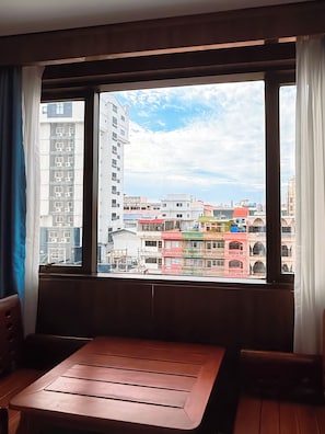 Una habitación con una mesa y sillas de madera, una ventana con cortinas y vistas a edificios coloridos.