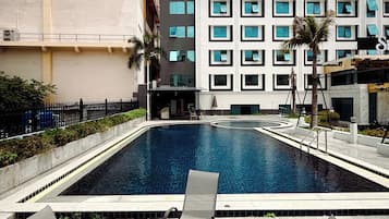 Ein Swimmingpool mit Liegestühlen und einem Tisch, umgeben von einem Gebäude mit mehreren Fenstern und Balkonen.
