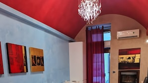 A modern living room with a red sofa, a dining table with chairs, a chandelier, and a fireplace. - Two-Room Apartment in Salento Historic Center (Galatina)
