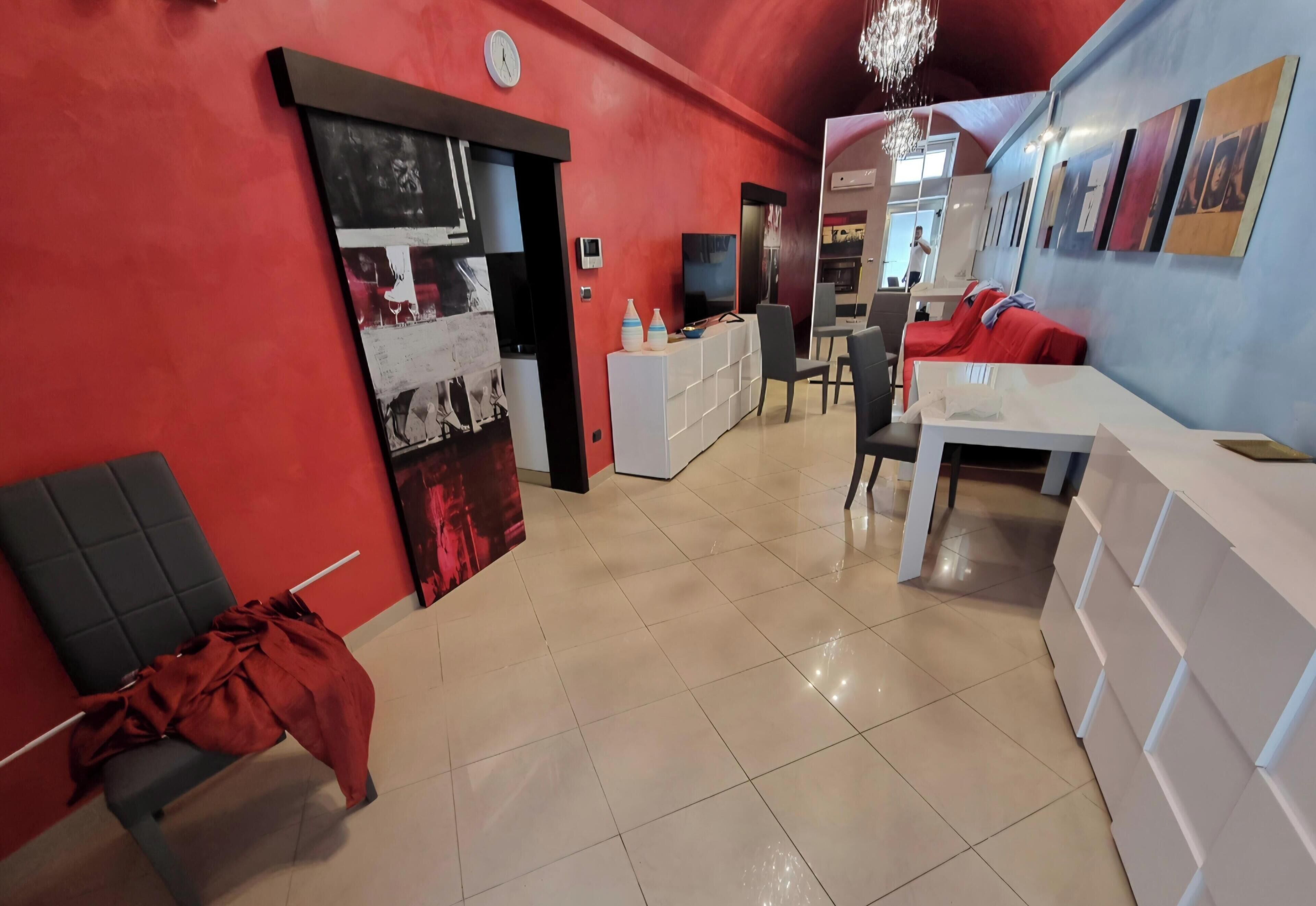 Una zona giorno moderna con una parete rossa a contrasto, un divano, un tavolo da pranzo e un angolo cottura con TV.