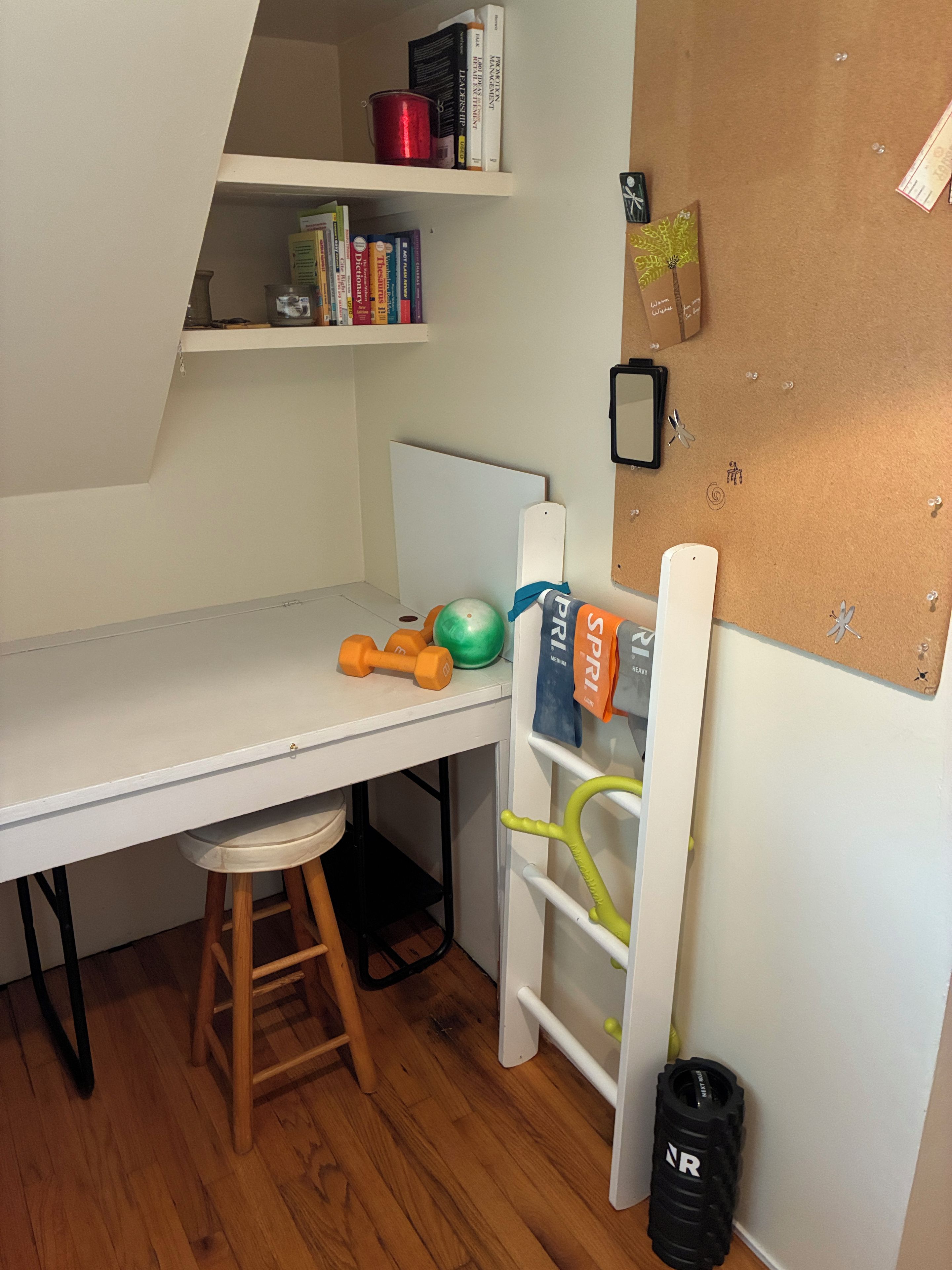 A child's room with a desk, a chair, a shelf with books, and a corkboard with some items pinned to it.