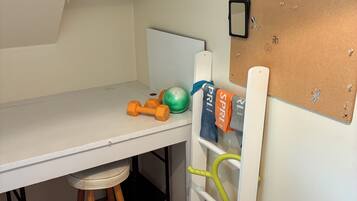 A child's room with a desk, a chair, a shelf with books, and a corkboard with some items pinned to it.
