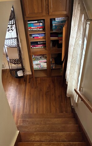 Una escalera de madera con un estante de juegos a la izquierda y una cortina a la derecha.