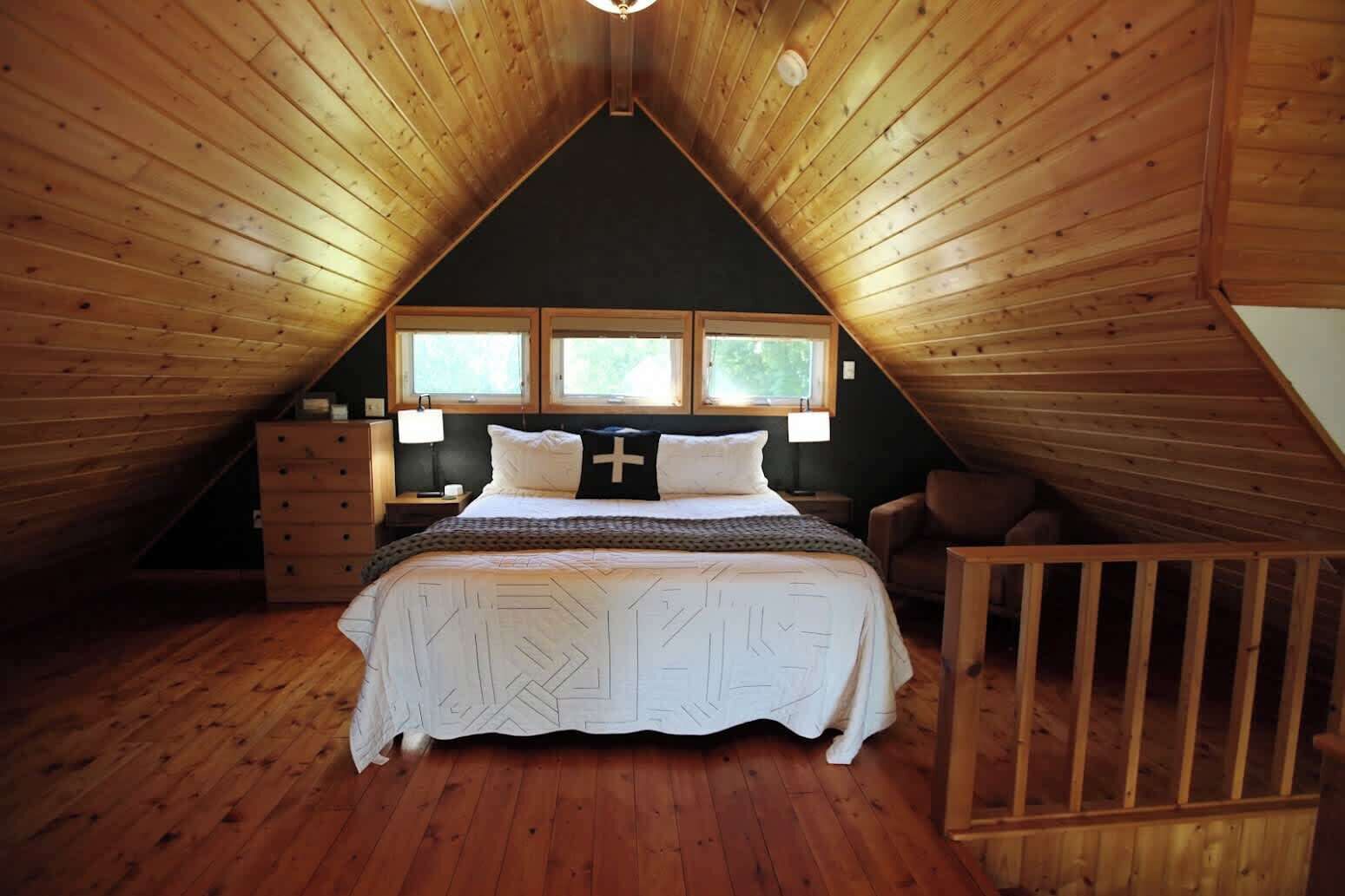 A bedroom with a sloped ceiling, a bed with a cross pillow, two bedside tables, and a window with a view.