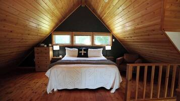 A bedroom with a sloped ceiling, a bed with a cross pillow, two bedside tables, and a window with a view.