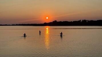 Un lac paisible au coucher du soleil, où trois personnes pêchent.
