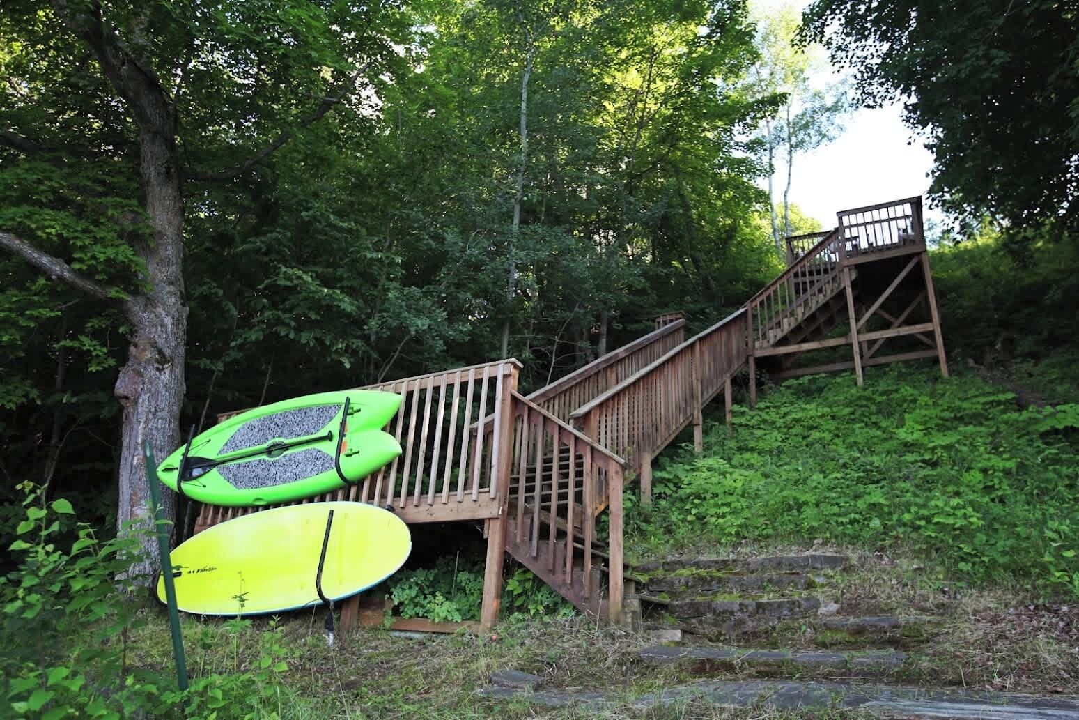 Una escalera de madera que sube una colina con dos kayaks apoyados al lado.