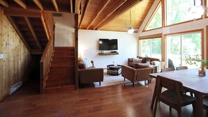 A wooden interior with a staircase, a living area with a sofa and TV, and large windows. - Leaf Lake Cabin, Henning MN (Henning)