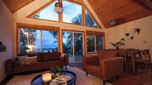 A cozy living room with a high ceiling, large windows, a sofa, a chair, a coffee table with magazines, and a candle. - Leaf Lake Cabin, Henning MN (Henning)