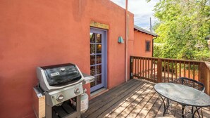 A barbecue grill, a table, and a deck with a wooden railing. - Charming Railyard Adobe, Pet Friendly (Santa Fe)