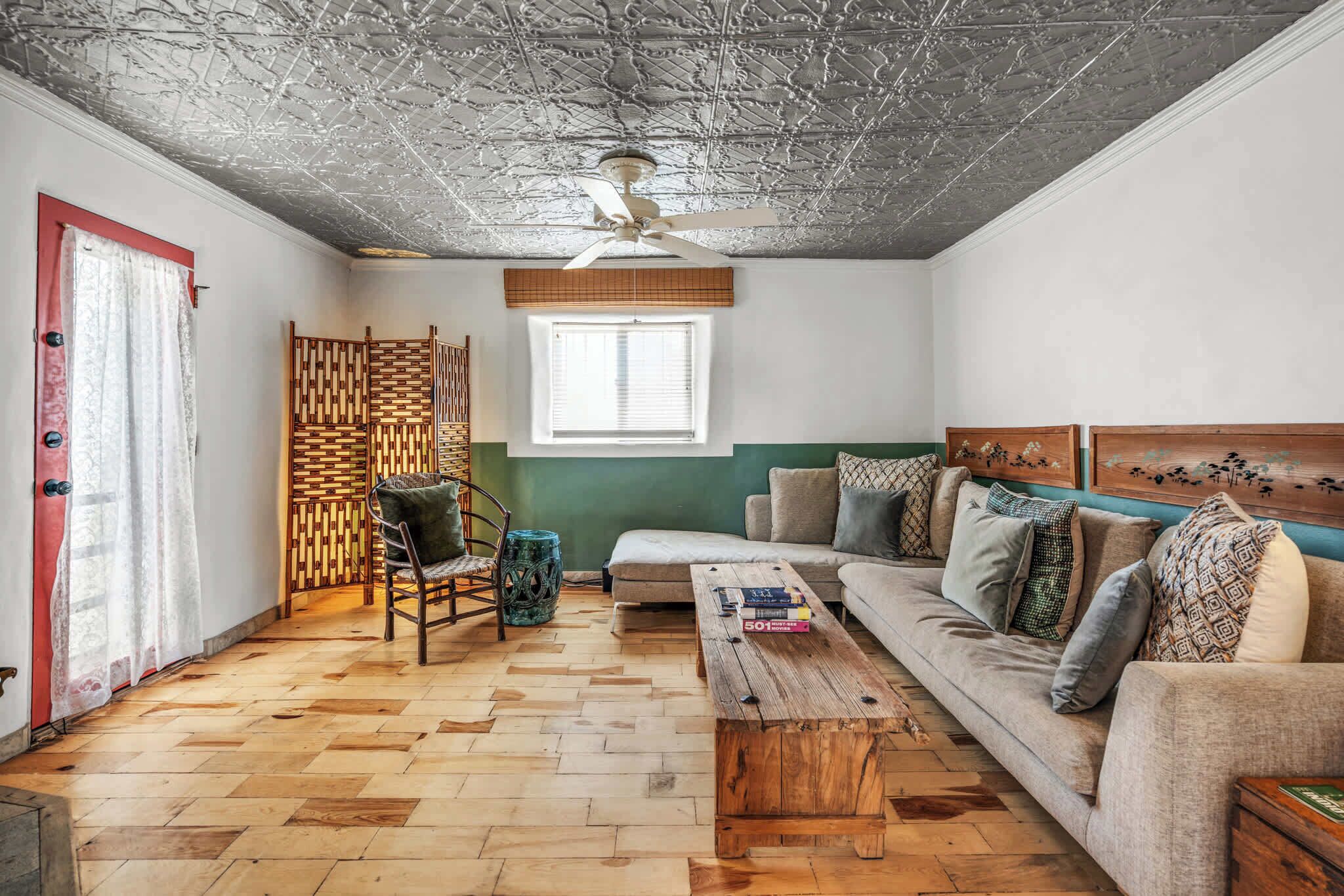 Olohuone, jossa on kalanruotokuviollinen lattia, sohva, sohvapöytä, tuoli, kattotuuletin ja ikkuna, jossa on sälekaihtimet.