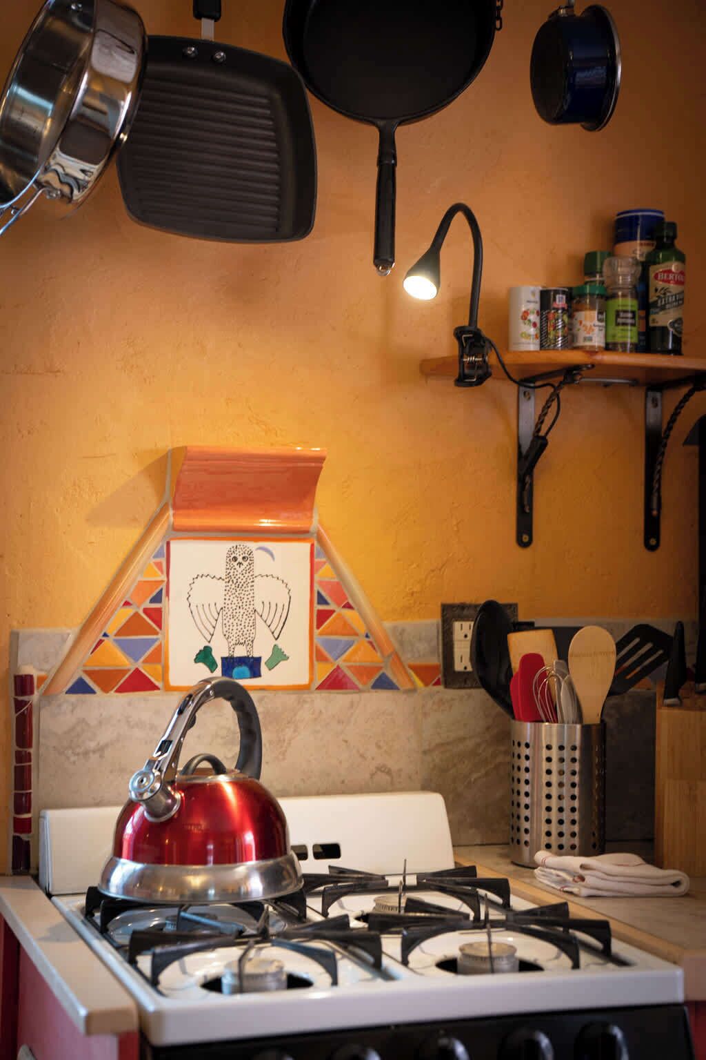 Een keuken met een gasfornuis, een waterkoker, een koekenpan en een plank met kruiden.
