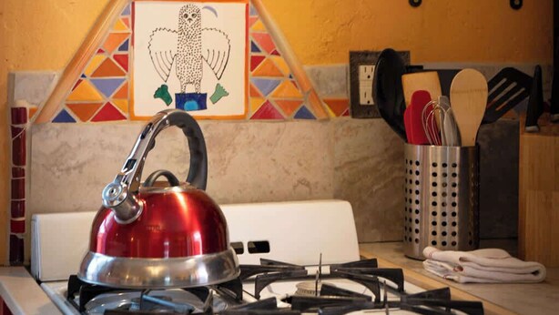 A kitchen with a gas stove, a kettle, a frying pan, and a shelf with spices. - Charming Railyard Adobe, Pet Friendly (Santa Fe)