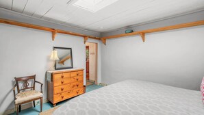 A bedroom with a bed, a wooden dresser, a chair, a mirror, and a skylight. - Charming Railyard Adobe, Pet Friendly (Santa Fe)