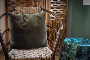 Ein Korbstuhl mit grüner Sitzauflage und ein kleiner Hocker mit blauer Sitzfläche.
