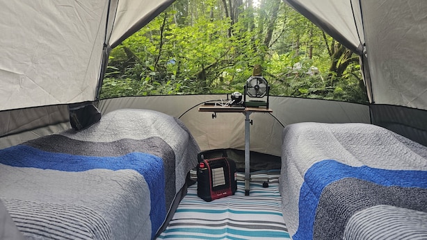 A tent with two beds, a fan, and a table with a power outlet.