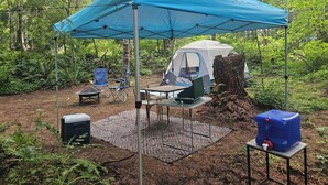 A campsite with a tent, a table, chairs, and a water dispenser.