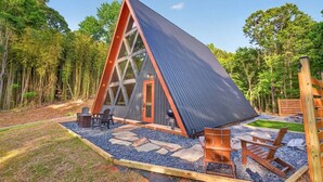 Une cabane triangulaire dotée d’une grande fenêtre, d’un espace salon extérieur et d’une terrasse en gravier.