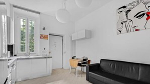 Una cuina moderna amb armaris blancs, una zona de menjador amb un sofà de pell negra i un quadre abstracte gran a la paret.