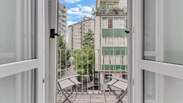 Un balcó amb vistes a edificis properes, una barana metàl·lica i un marc de porta.