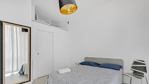 Un dormitori amb un llit, una cadira, un mirall i una làmpada penjant.