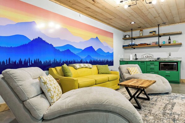A living room with a mountain mural, green cabinets, and a yellow sofa.