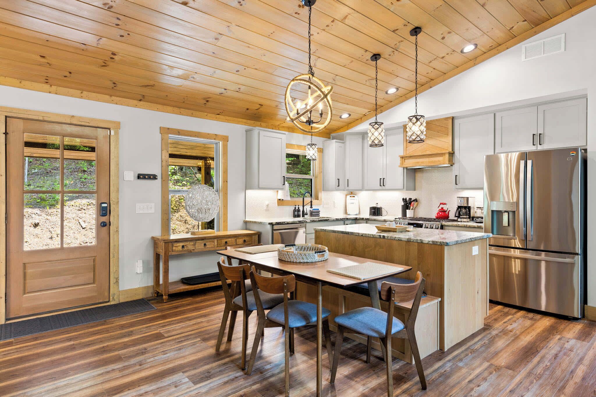 Une cuisine moderne avec un plafond en bois, des appareils en acier inoxydable et un coin repas comprenant une table et des chaises en bois.