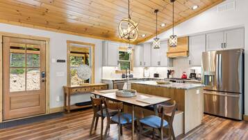 Une cuisine moderne avec un plafond en bois, des appareils en acier inoxydable et un coin repas comprenant une table et des chaises en bois.