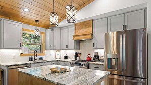 Eine moderne Küche mit Granitarbeitsplatten, Edelstahlgeräten und Holzbalken an der Decke.