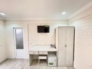 A room with a white brick wall, a wooden cabinet, a desk with drawers, a small cabinet, and a door. - Hotel Zarina (Samarkand)