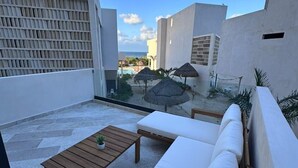 Een dakterras met een witte bank, houten tafel en rieten parasols.