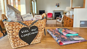 Un panier en osier orné d’une étiquette en forme de cœur sur laquelle est inscrit : « Avec nos meilleurs vœux », et une pile de livres posée sur une table.