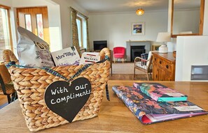 A wicker basket with a heart-shaped label reading 'With our compliments' and a stack of books on a table. - Lochside - sleeps 6 guests  in 3 bedrooms (Dornie)