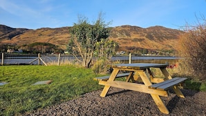 Une table de pique-nique installée dans un espace verdoyant, avec un lac et des montagnes en arrière-plan.