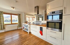 A kitchen with white cabinets, a wooden countertop, a built-in oven, and a view of the outdoors through large windows. - Lochside - sleeps 6 guests  in 3 bedrooms (Dornie)