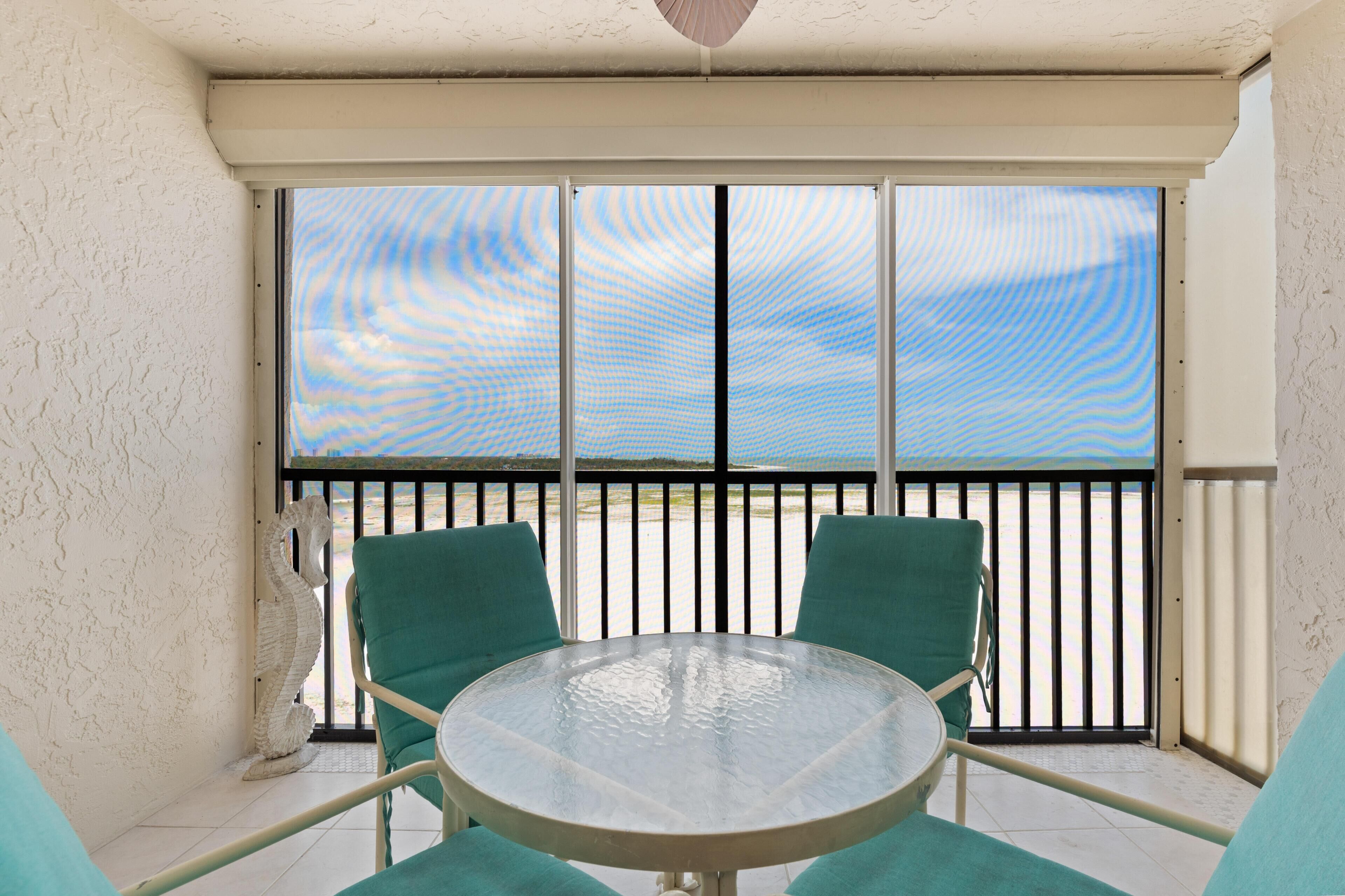 Un balcon avec une table et des chaises en verre, une vue sur la plage et une décoration représentant un hippocampe blanc.
