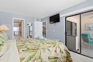 Een slaapkamer met een bed, een televisie, een schuifpui naar een balkon en een badkamer zichtbaar door een geopende deur.