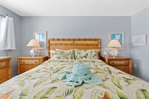A bedroom with a bed, two nightstands, a wooden headboard, a floral bedspread, a towel, and two wall-mounted lamps. - Carlos Pointe #534 Heavenly Sunsets (Fort Myers Beach)