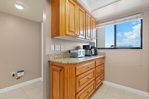 A kitchen with wooden cabinets, a countertop with appliances, and a window with a view. - Carlos Pointe #534 Heavenly Sunsets (Fort Myers Beach)