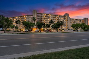 Ein mehrstöckiges Hotel mit schlichter Fassade, vielen Fenstern und einem Parkplatz mit Autos.