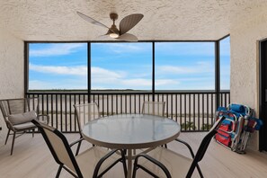 A balcony with a table and chairs, a ceiling fan, and a view of the beach. - Carlos Pointe #231 Beach Bum Getaway (Fort Myers Beach)