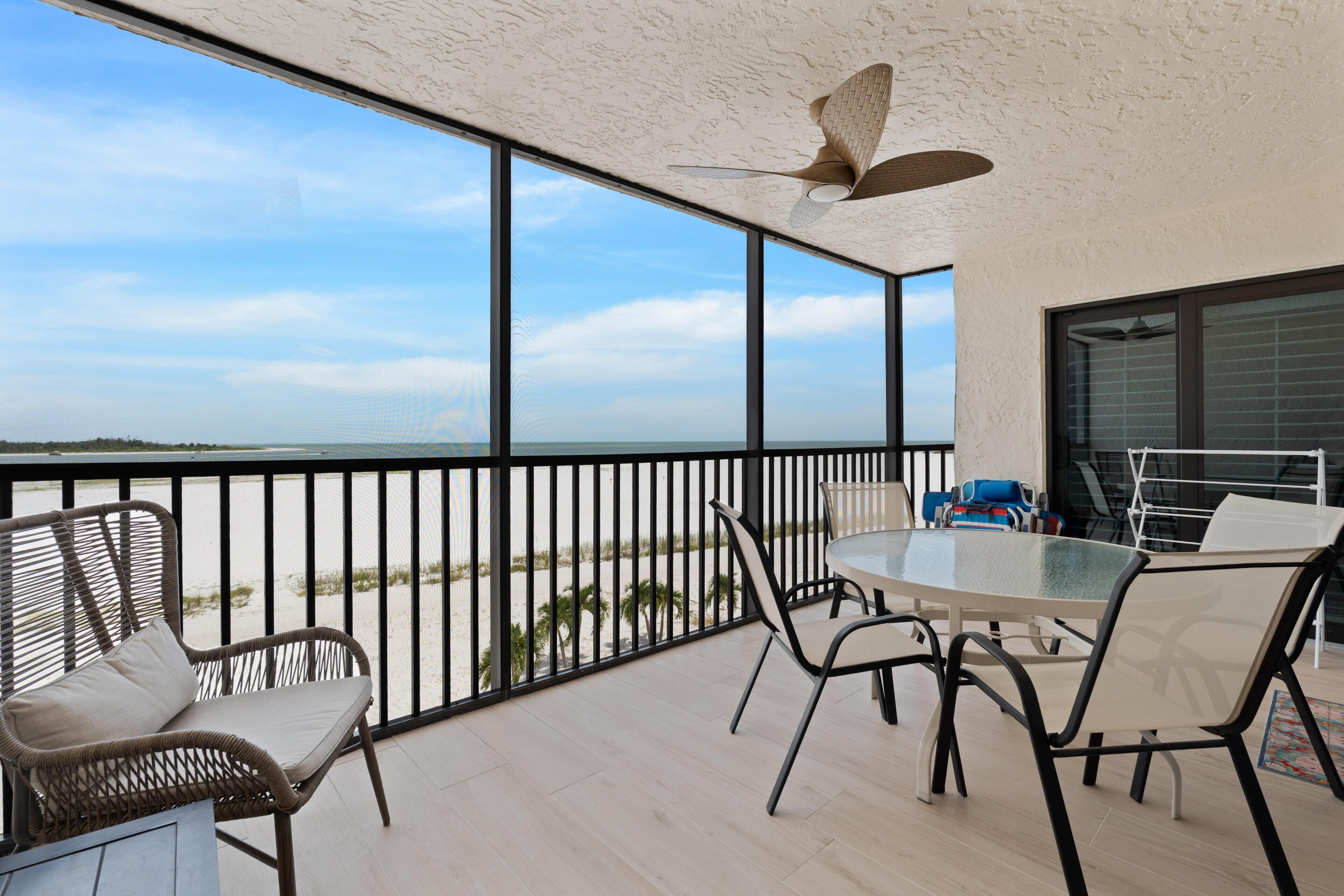 Ein Balkon mit Blick auf den Strand, einem Tisch mit Stühlen und einem Deckenventilator.